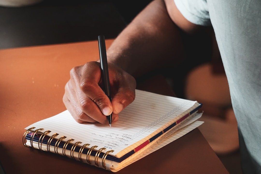 Hand writing in a notebook with a black pen.